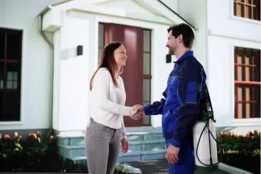 Un agent antiparasitaire sympathique et une femme heureuse se serrent la main à l'extérieur de la maison.